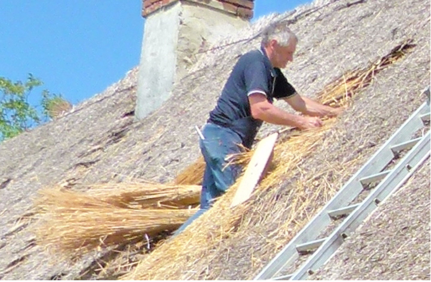 Prikaz pokrivanja hiše s slamnato streho in popravljanja zidu z ilovnatim ometom